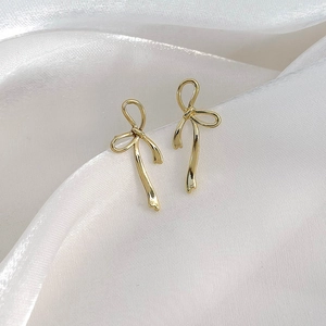 Elegant gold bow-shaped ribbon dangle earrings displayed on white silk fabric background