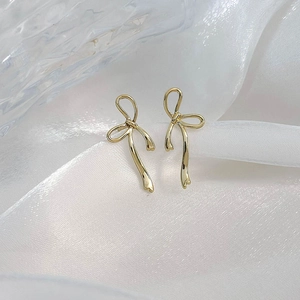 Detail of 18K gold bow ribbon stud earrings on white silk and glass background