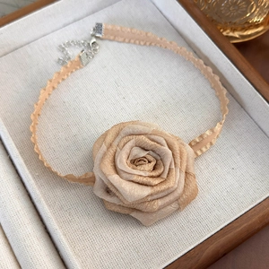 Detail of beige fabric rose choker necklace with elegant ribbon texture on a linen tray