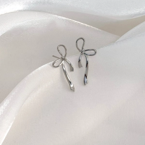 Close-up of elegant silver bow ribbon stud earrings on a textured white silk background