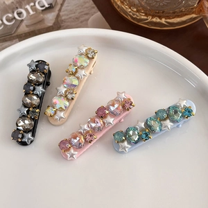 Star hair clips set with pink gems and pearls in a white dish, 45-degree angle view