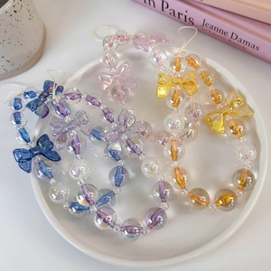 Colorful iridescent beaded phone charm strap with bow ties on white ceramic display plate