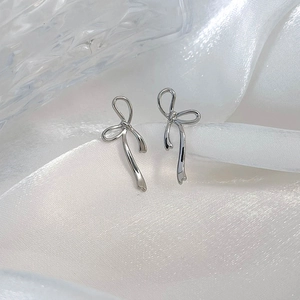 Close-up of elegant silver bow earrings with a polished mirror finish on white silk