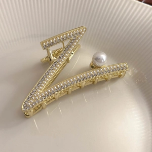 Détail d'une pince à cheveux lettre V dorée ornée de perles blanches et de strass brillants