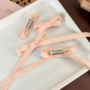 Detail of peach ribbon bow hair clips with long streamers on a white ceramic tray