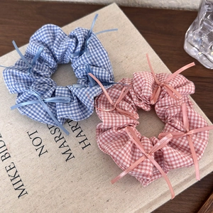 Close-up of blue and pink plaid hair scrunchies with bow details on a book surface