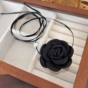Close-up of black fabric rose choker with a white pearl in a wooden jewelry box