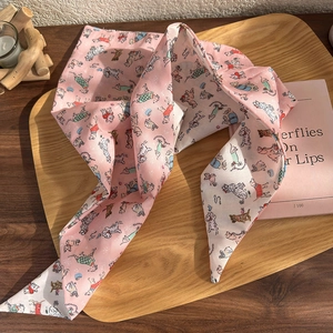 Cute pink dog print narrow silk scarf shown on a wooden tray with a cozy home setting