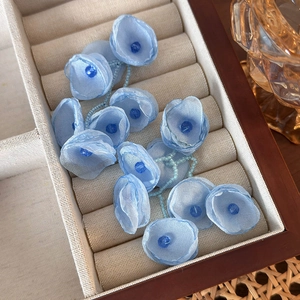 Close-up of light blue mesh flower earrings with delicate blue beads in a wooden box