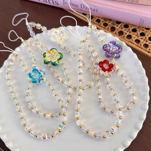 Detail showing five colorful crystal flower phone charms in a white ceramic dish