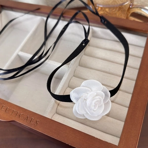 Detail of a handmade white satin camellia flower on a minimalist black ribbon choker