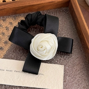 Dettaglio dell'elastico nero con fiocco di raso e rosa di stoffa bianca su vassoio in legno
