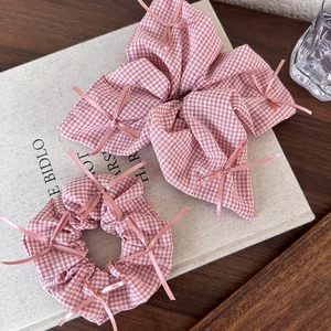 Close-up of pink checkered bow scrunchie with delicate ribbon detailing on a textured base