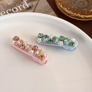 Close-up of pink and blue star hair clips with pearls and crystals in a white ceramic dish