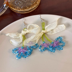 Detailed shot of mesh flower earrings with blue bead charms in a ceramic dish
