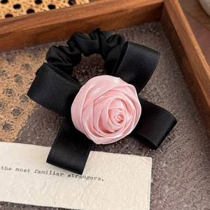 Dettaglio di una rosa in raso rosa e un fiocco nero su un elastico per capelli elegante