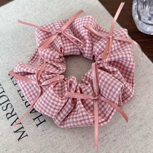 Detailed view of pink plaid scrunchie with silk bows on textured fabric background