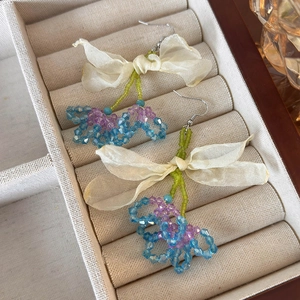Detail of handmade tulle flower earrings with green beads and blue crystal on fabric