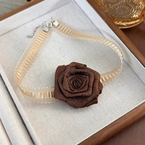 Close-up of a vintage brown fabric rose choker with delicate gold ribbon in a jewelry tray