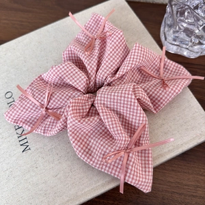 Detail of a pink checkered scrunchie with delicate bow accents on a book surface