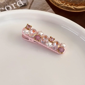 Detail view of pink hair clip with sparkling crystals and star pearl on a ceramic plate