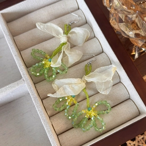 Detail of floral crystal bead earrings with cream bows on a beige velvet jewelry tray