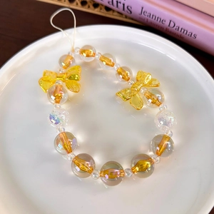 Detail of yellow iridescent beads and bright bow charms on a decorative mobile phone strap