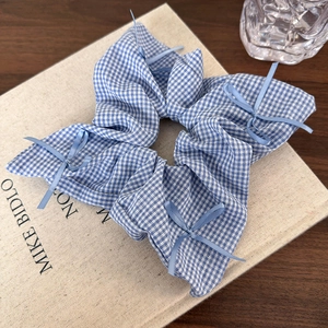 Close-up of blue gingham scrunchie with delicate ribbon bows on a textured background