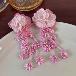 Detail of pink chiffon flower earrings with beaded tassel rings on a cream ceramic plate