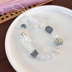 Détail de la dragonne de téléphone en perles avec papillons bleus dans un plateau en céramique