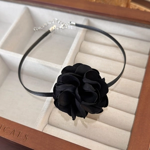 Close-up of a black fabric camellia choker necklace on a premium jewelry box
