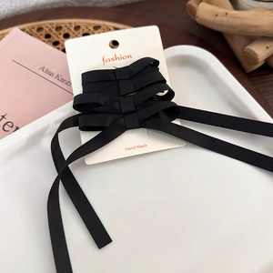Detailed view of handmade black ribbon bow hair clips with long streamers on a white card