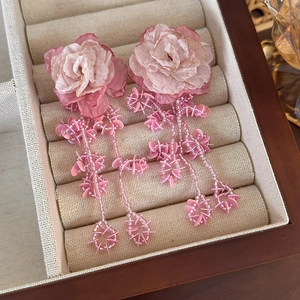 Detail of pink mesh flower tassel earrings with shimmering beads and sequins on beige linen