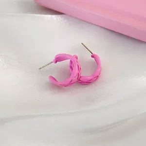 Pink C-shape twist hoop earrings with diamond pattern texture on white silk background