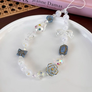 Détail d'une dragonne de téléphone perlée avec fleurs et papillons en résine sur plat blanc