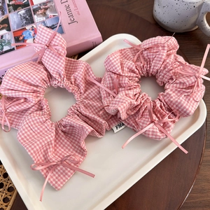 Detail of pink plaid hair scrunchies with satin bows and woven FMa label on a white tray