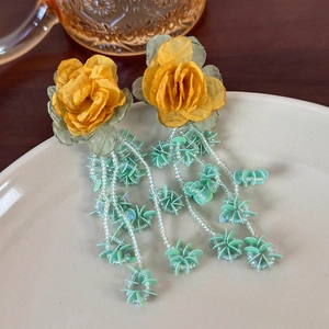 Detail of bohemian yellow fabric rose earrings with green leaves and mint green beaded tassels