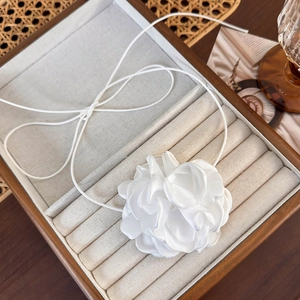 Détail d'un ras-de-cou fleur en tissu blanc posé sur un coffret à bijoux en bois
