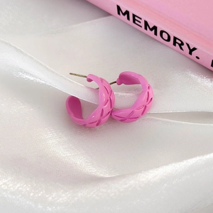 Macro shot of pink C-shaped quilted hoop earrings on a decorative silk and book background