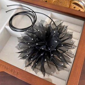 Detail view of a black mesh flower choker with silver rhinestones in a wooden jewelry box