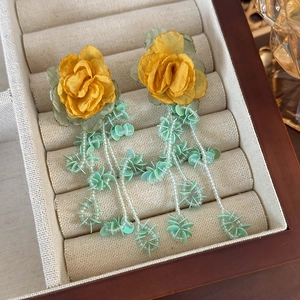 Detail of vintage fabric yellow rose earrings with green beaded tassels in a jewelry box