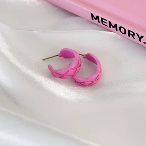 Detail view of pink quilted C-shape hoop earrings on white silk background texture