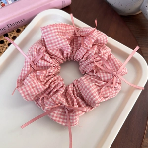 Detailed close-up of a pink and white plaid scrunchie with silk bow accents
