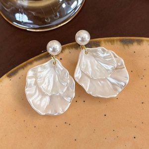 Eleganti orecchini di perle bianche con petali di madreperla su un piatto di ceramica beige