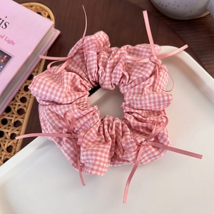 Detail of pink gingham scrunchie with satin bows on a minimalist white tray