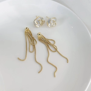 Détail de boucles d'oreilles camélia françaises avec chaînes à pompons dorées sur assiette blanche