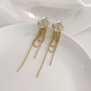 Vue macro des boucles d'oreilles camélia français avec pompons dorés et détails floraux