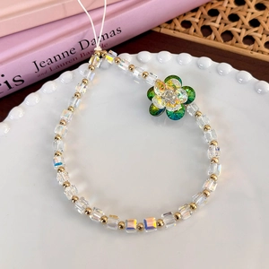 Close-up of beaded phone strap with square glass beads and crystal flower on a ceramic plate
