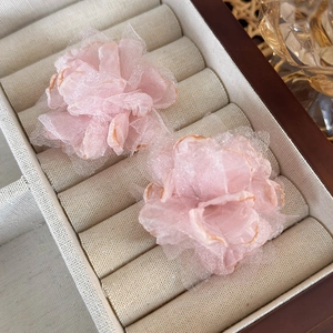 Detail view of pink organza flower earrings on a beige textile jewelry display box
