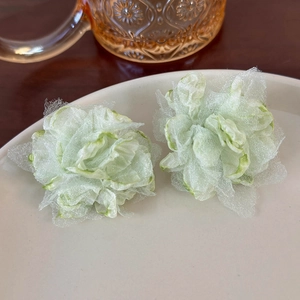 Detail shot of light green sheer mesh flower earrings on a minimalist white ceramic plate